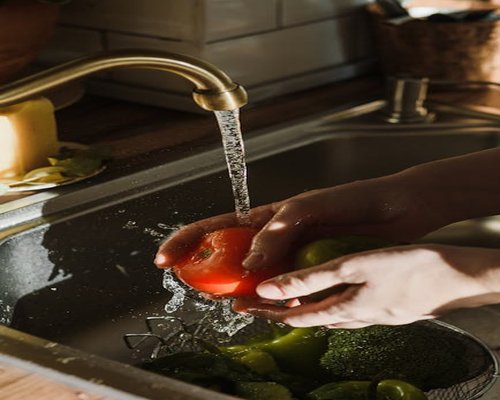 Fresh vegetables being washed in a kitchen sink